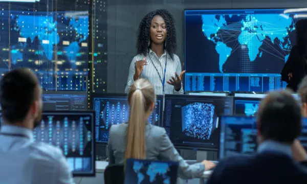 A data scientist speaks to a group with screens containing global data behind her.
