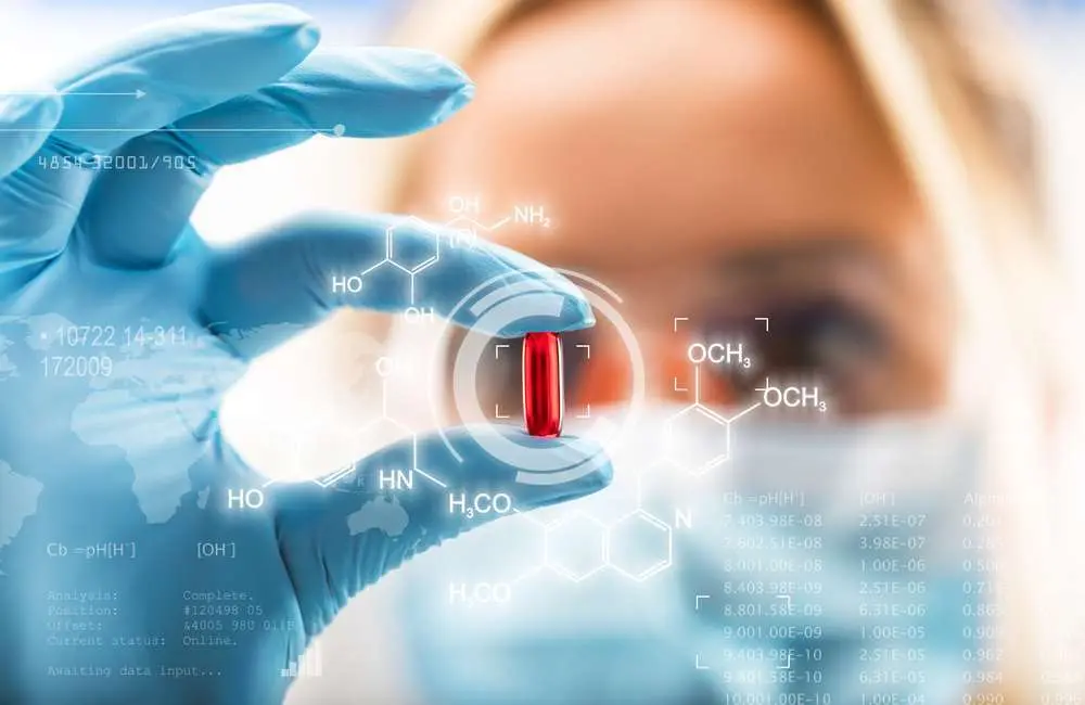 A healthcare professional wearing gloves holds up a red pill.
