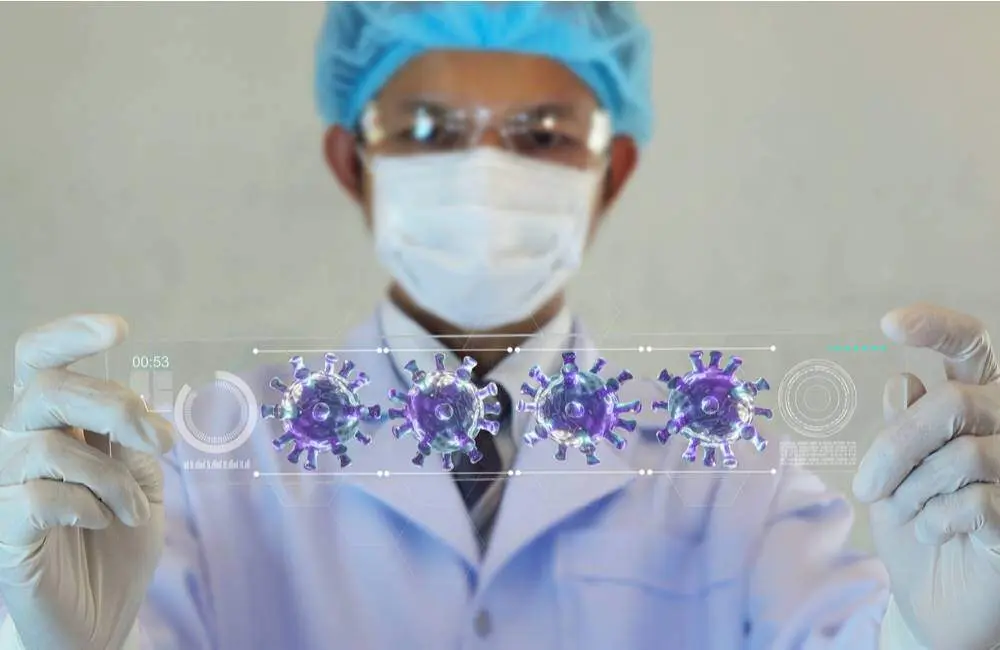 A healthcare professional wearing a mask and gloves holds up a microscope slide containing oversized Covid-19 molecules.