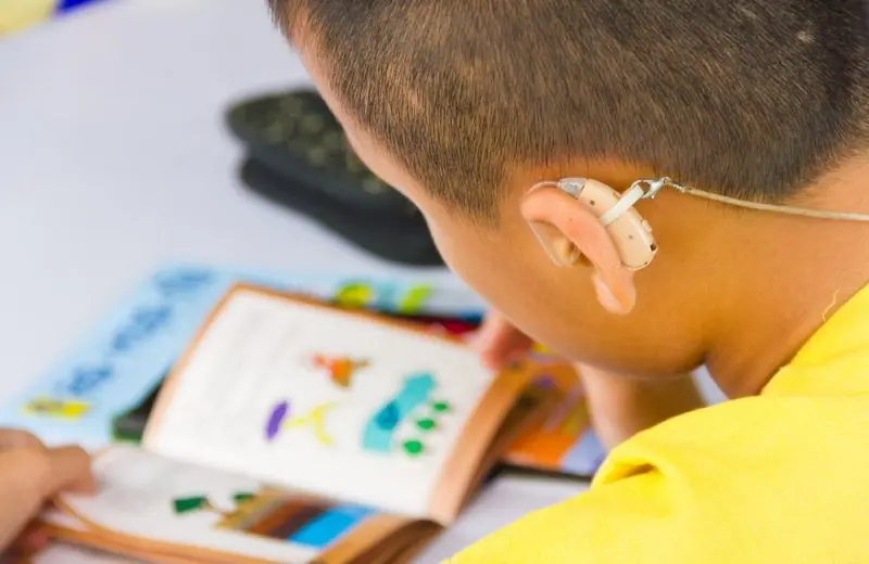 A closeup of a hearing aid on a young student who is reading a book.