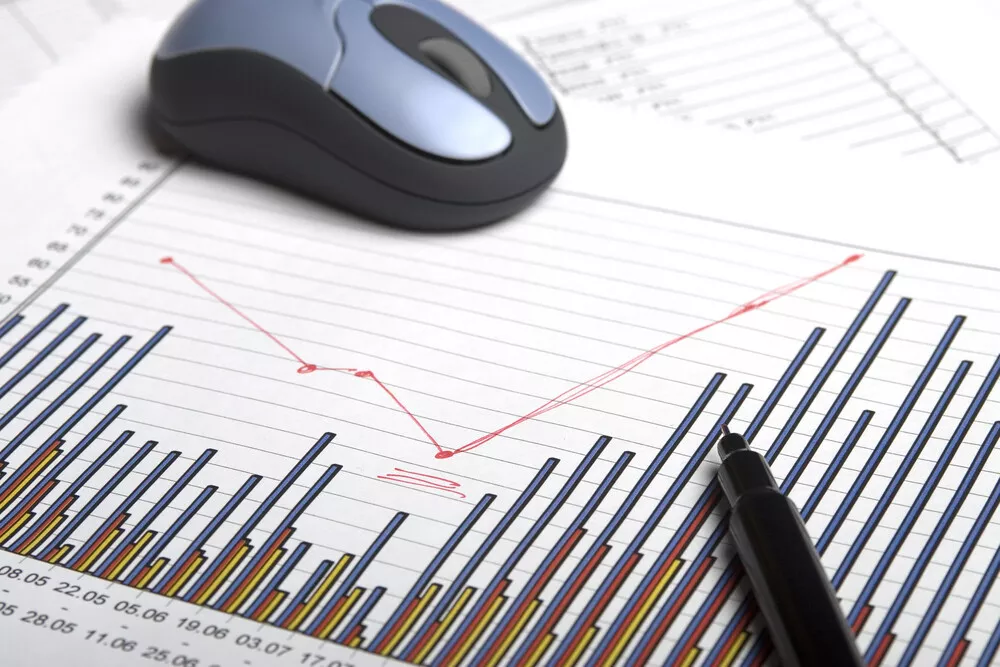A computer mouse and a pen sit on top of a document with a bar chart and line graph on it.