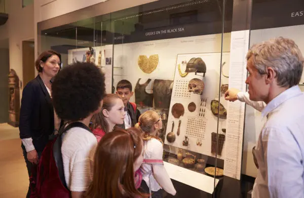 A museum guide speaks to a group of students in front of an exhibit.