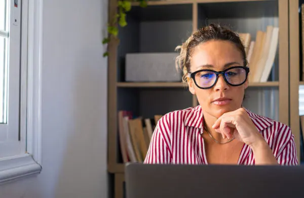 A woman wearing glasses works on a laptop.