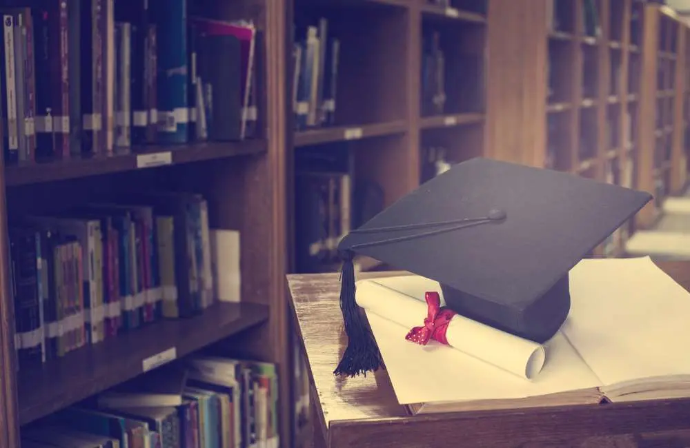 A graduation cap and diploma lay on a podium in a library.