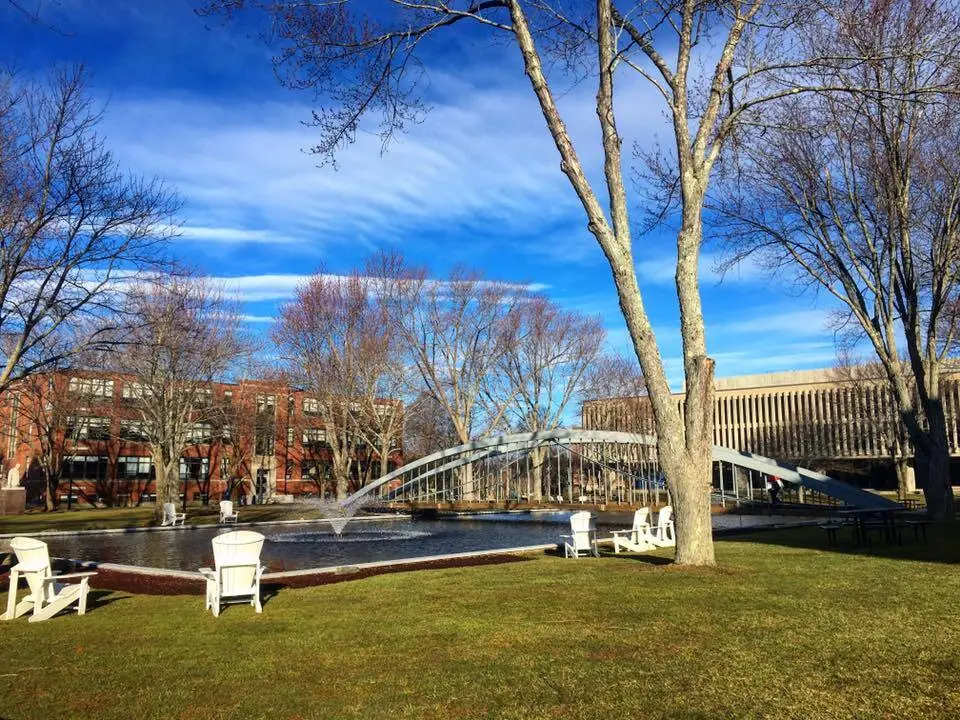 A landscape view of a bridge across a pond with fountains on the Merrimack College campus.