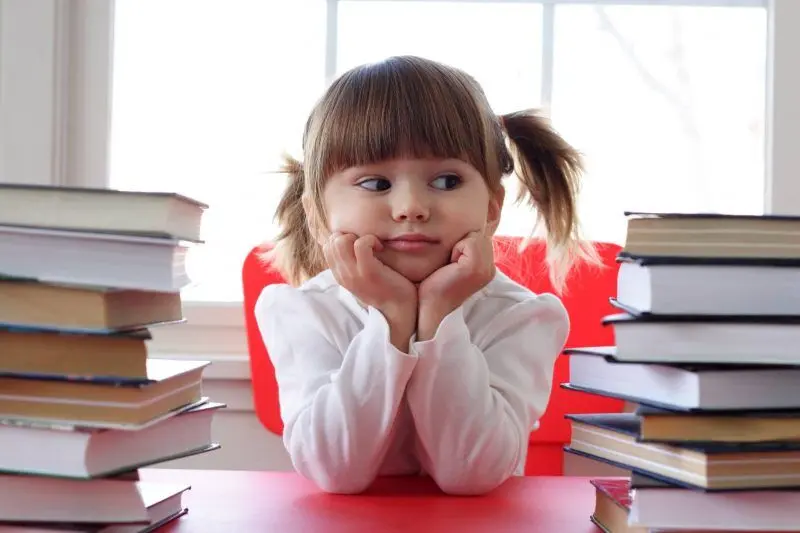 A young child sits between tall stacks of books.