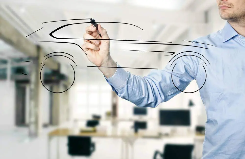 A product manager draws a car with a dry erase marker on a transparent screen, facing the viewer.