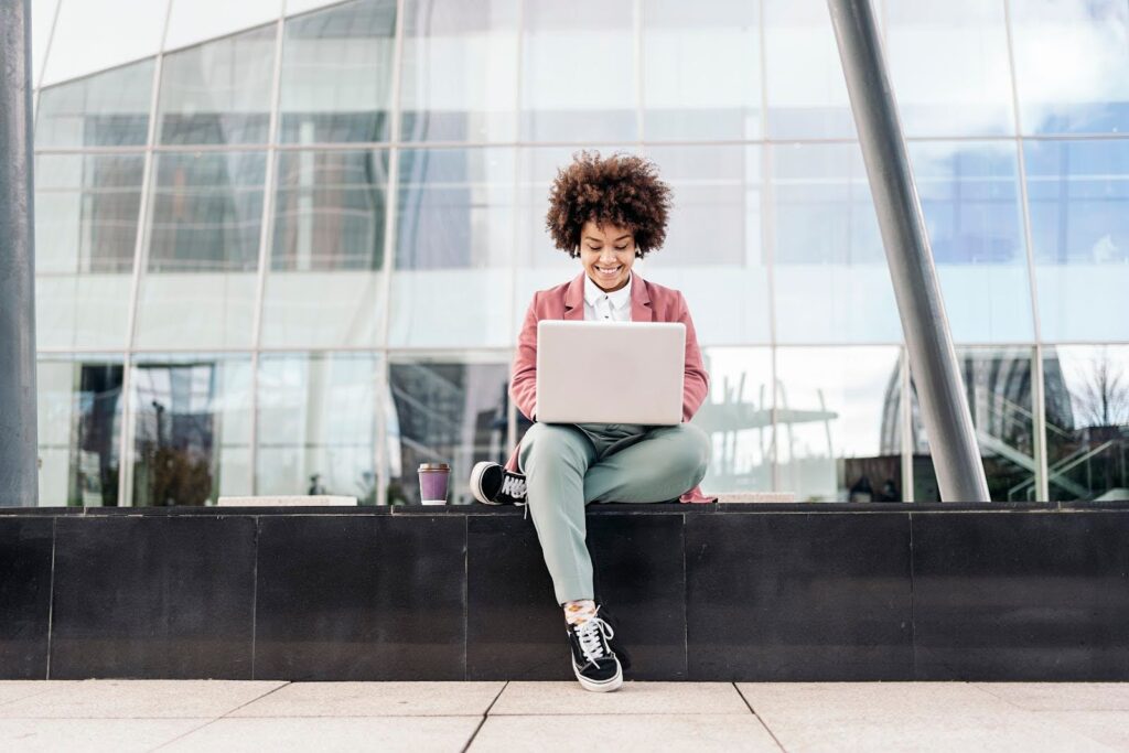 A woman seated outdoors in an office park types on a laptop computer.