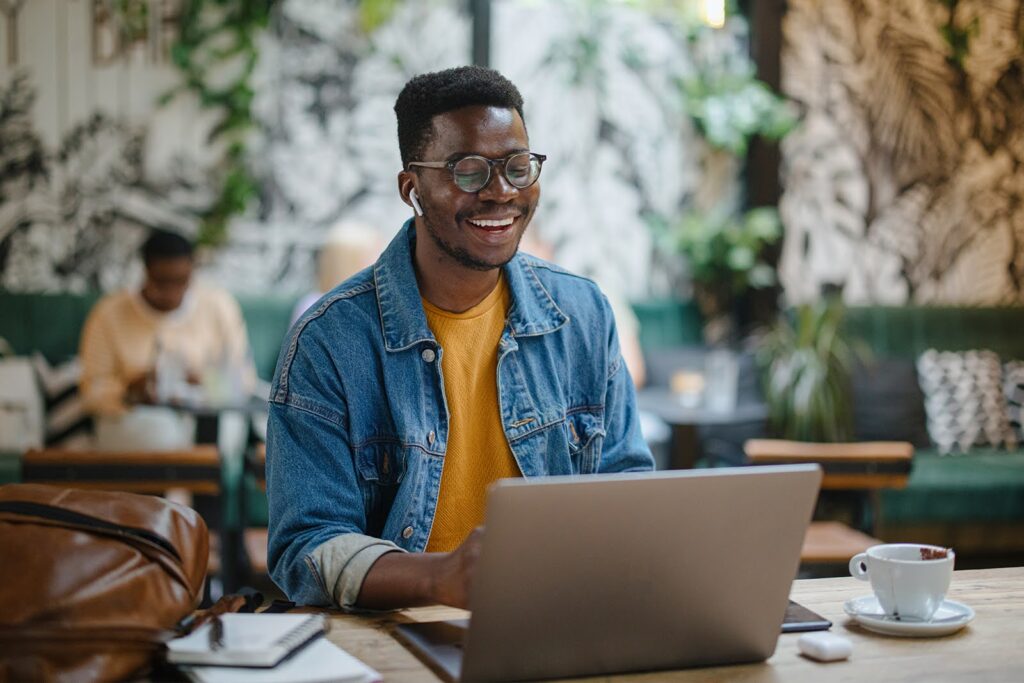 A smiling young man in a cafe works at a laptop computer.