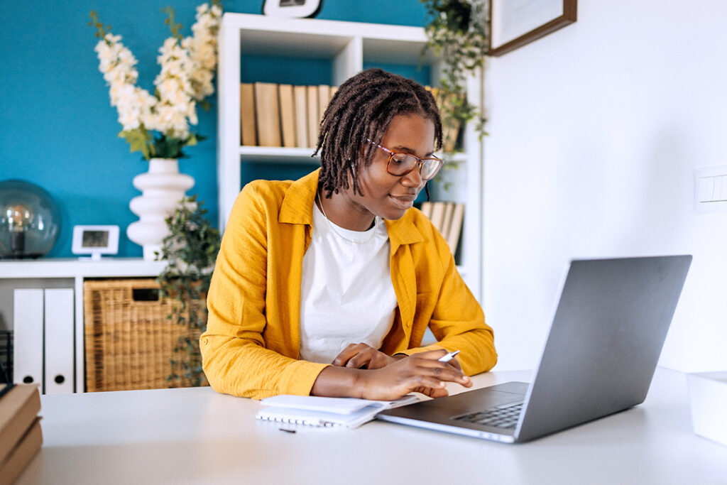 A woman in a yellow blazer works at a laptop.