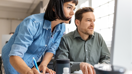 Two data scientists consult a computer screen while taking notes.