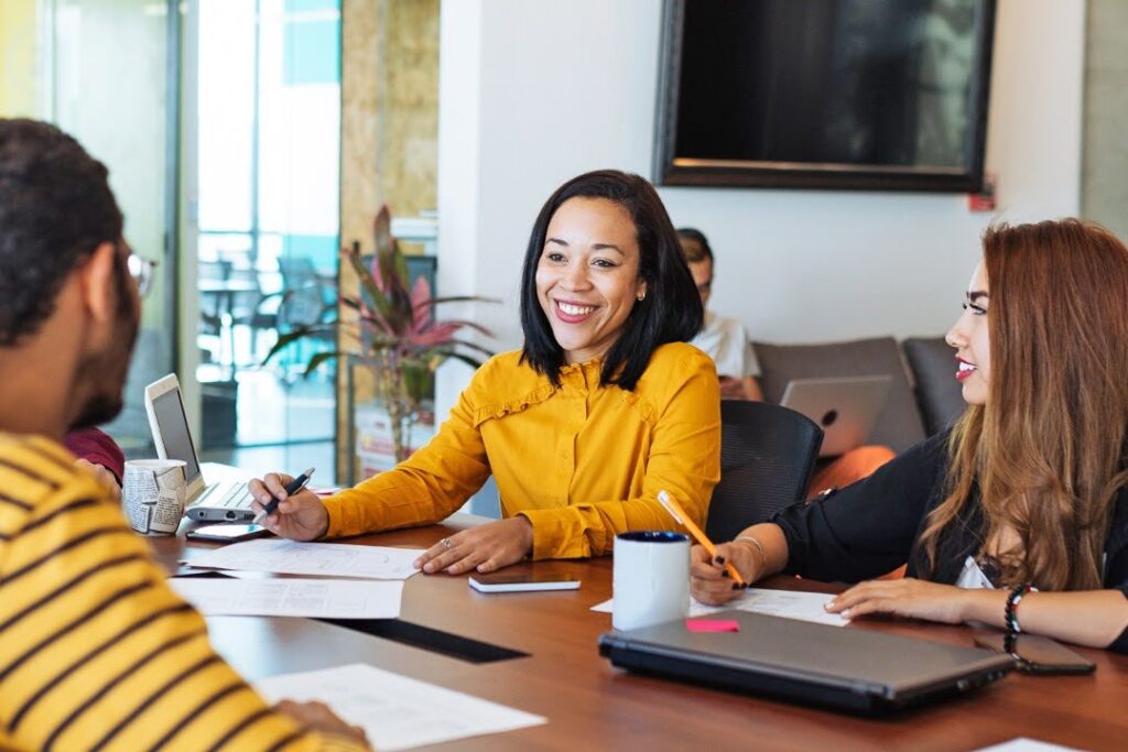 Three people sit at a conference table, engaged in a meeting.